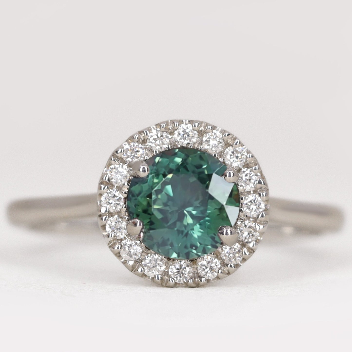 Round cut teal sapphire engagement ring with white diamond halo in platinum