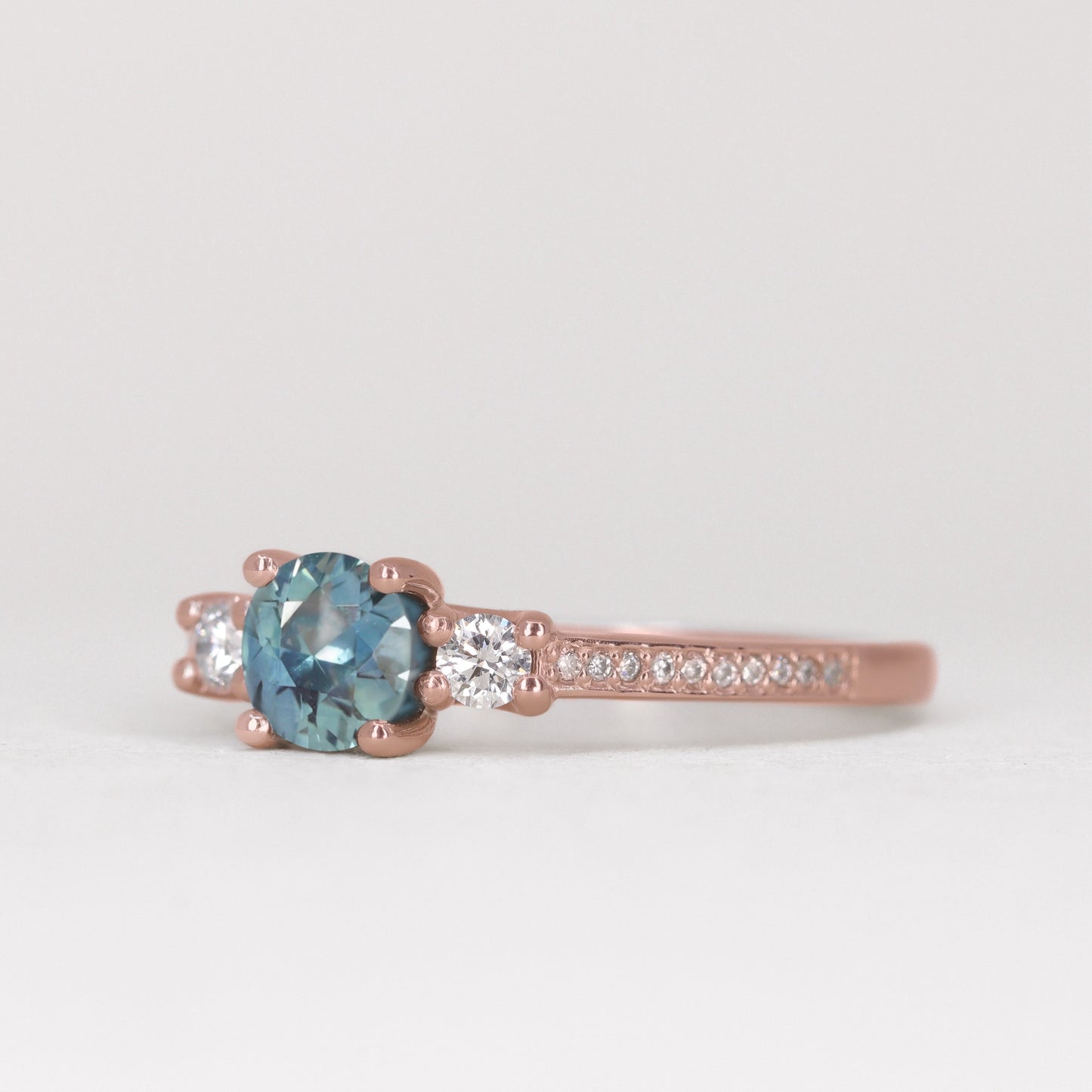 Round cut teal sapphire trilogy engagement ring with pave band