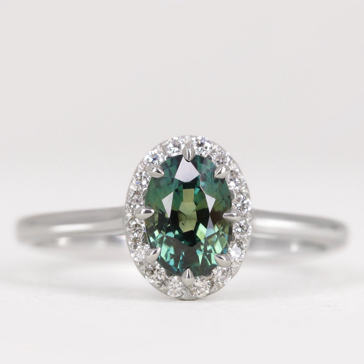 Oval cut teal sapphire with diamond halo engagement ring in platinum