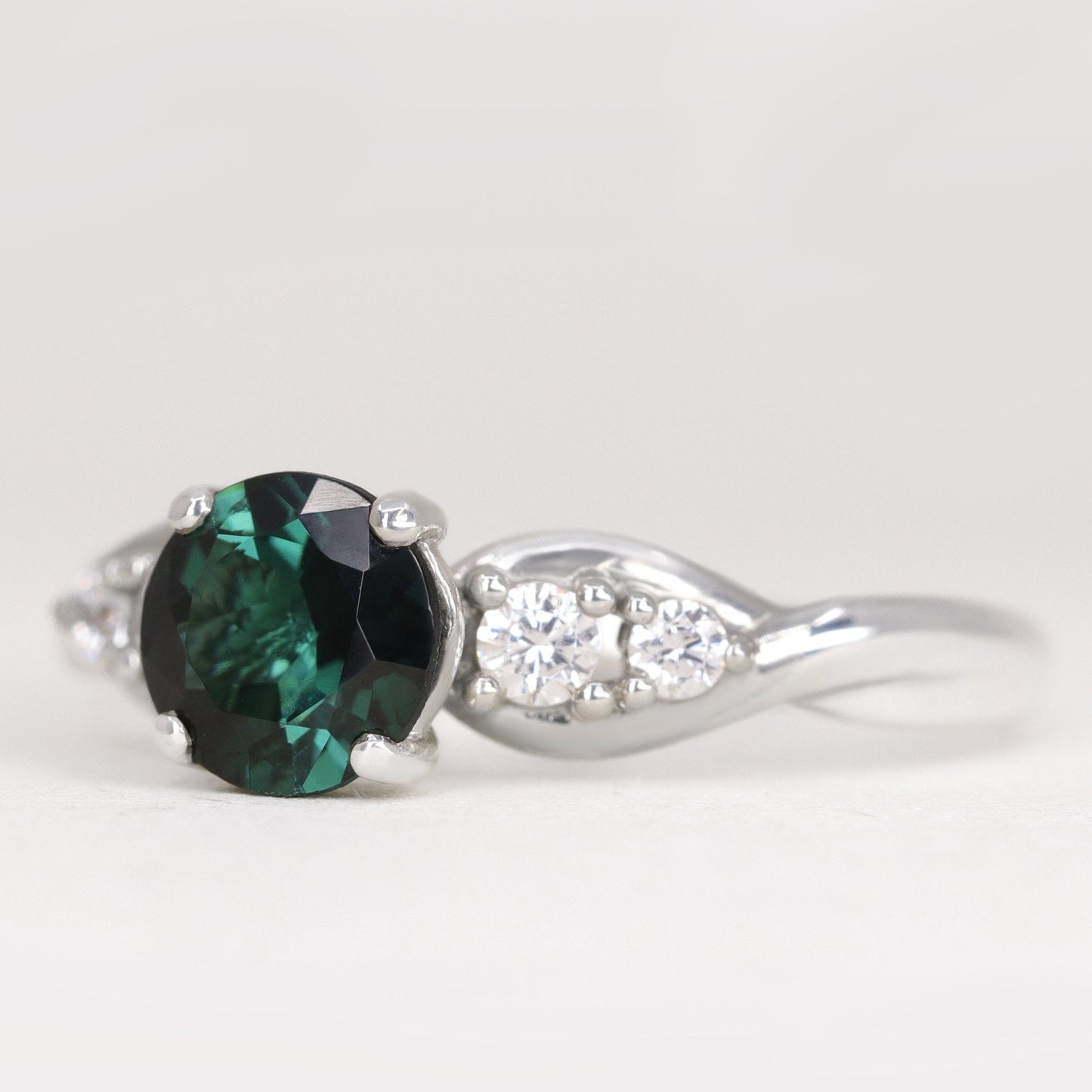 Round cut teal sapphire and white diamond engagement ring in platinum