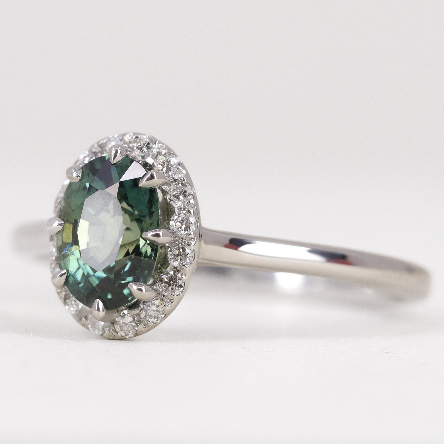 Unique oval cut teal sapphire with diamond halo engagement ring in platinum